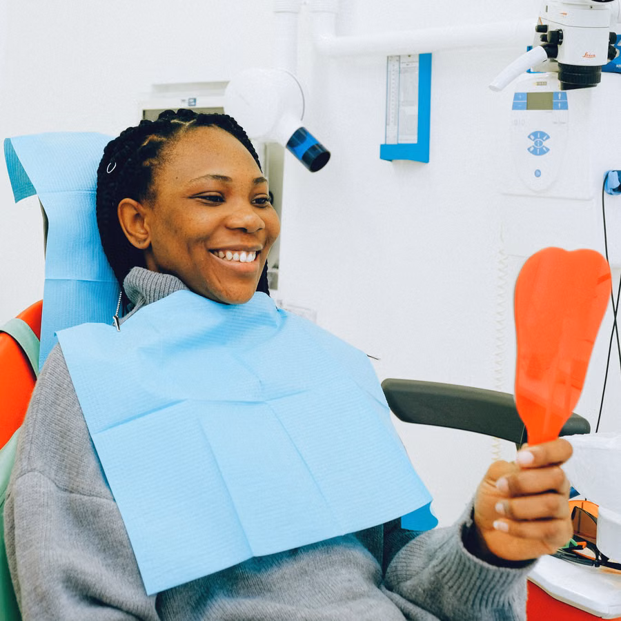 A patient smiling at her reflection in a hand mirror after a dental visit